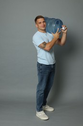 Photo of Smiling delivery man with cooler bottle of water on grey background