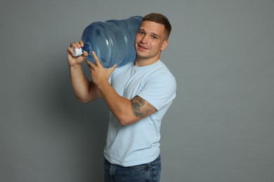 Photo of Smiling delivery man with cooler bottle of water on grey background