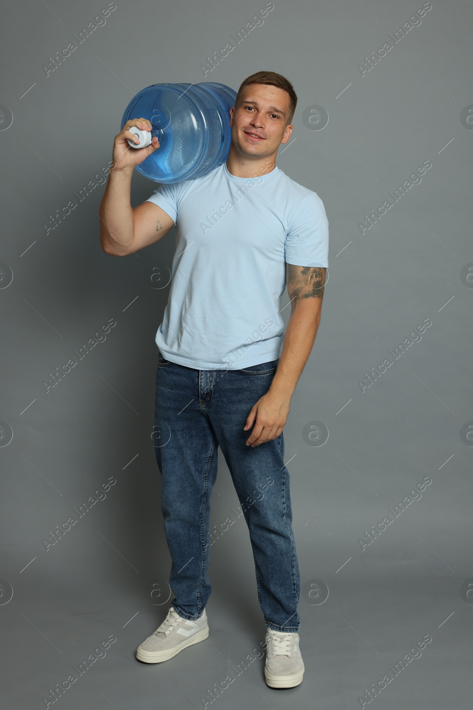 Photo of Smiling delivery man with cooler bottle of water on grey background