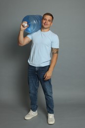 Photo of Smiling delivery man with cooler bottle of water on grey background