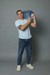 Photo of Smiling delivery man with cooler bottle of water on grey background