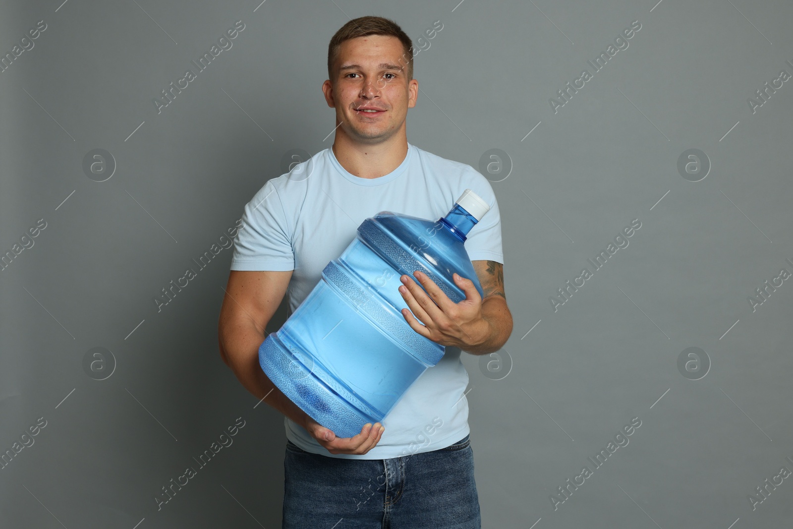 Photo of Smiling delivery man with cooler bottle of water on grey background