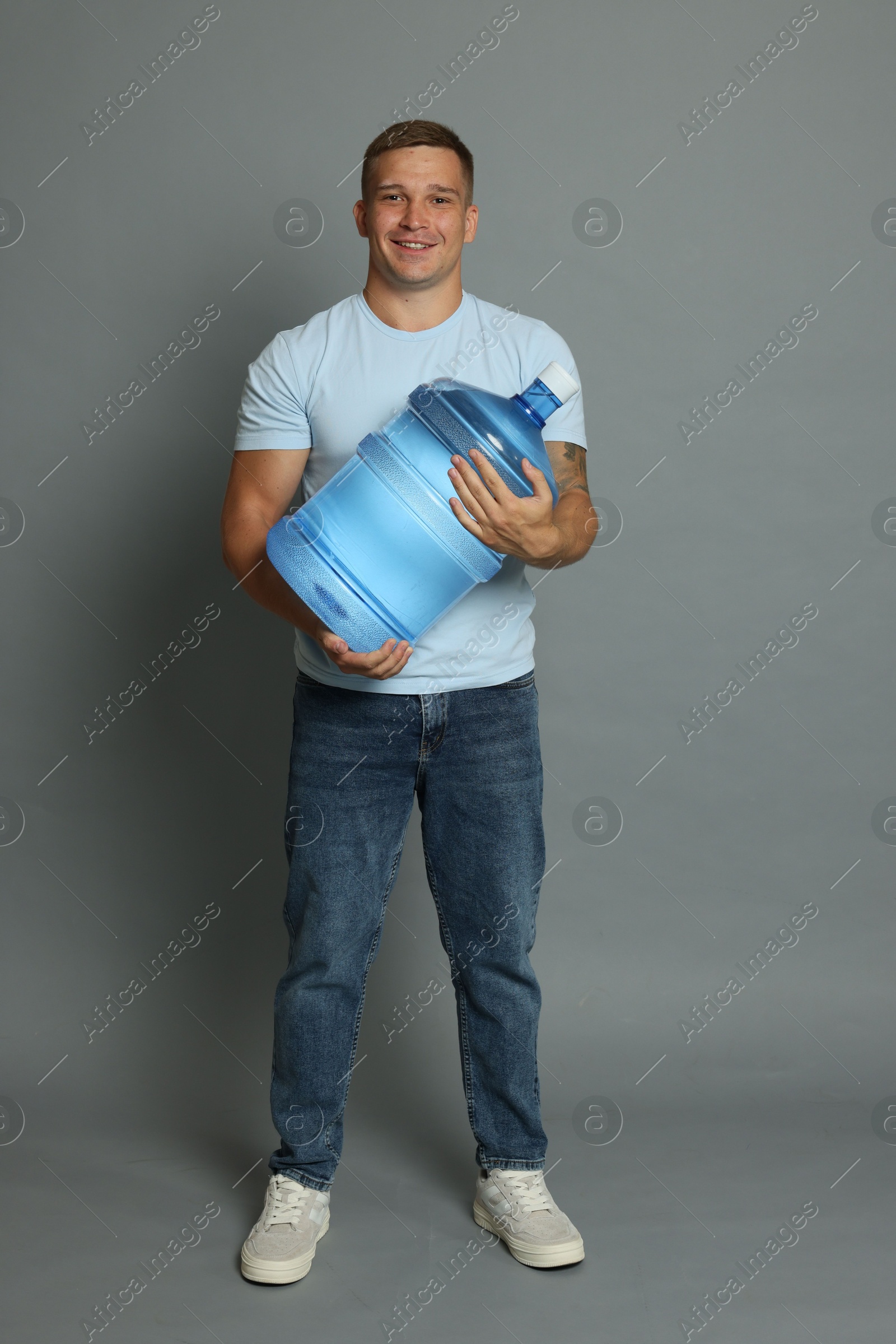 Photo of Smiling delivery man with cooler bottle of water on grey background