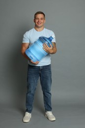 Photo of Smiling delivery man with cooler bottle of water on grey background
