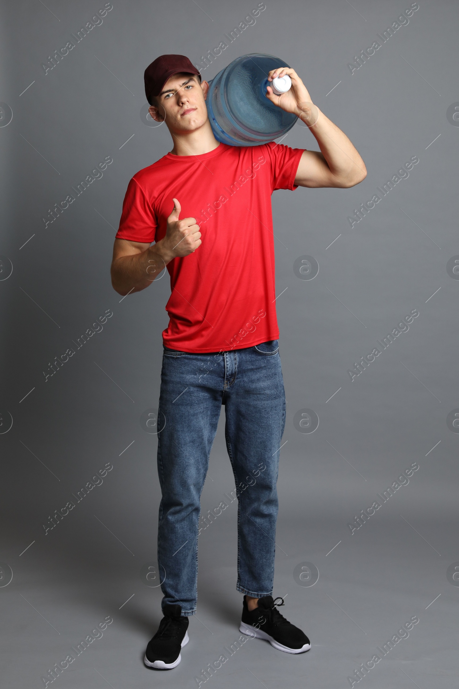Photo of Delivery man with cooler bottle of water showing thumbs up on grey background