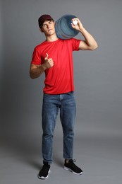 Photo of Delivery man with cooler bottle of water showing thumbs up on grey background