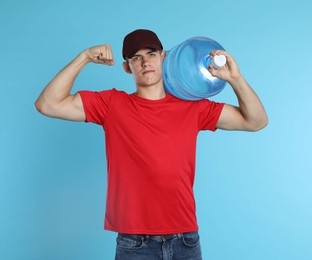 Photo of Delivery man with cooler bottle of water showing his biceps on light blue background
