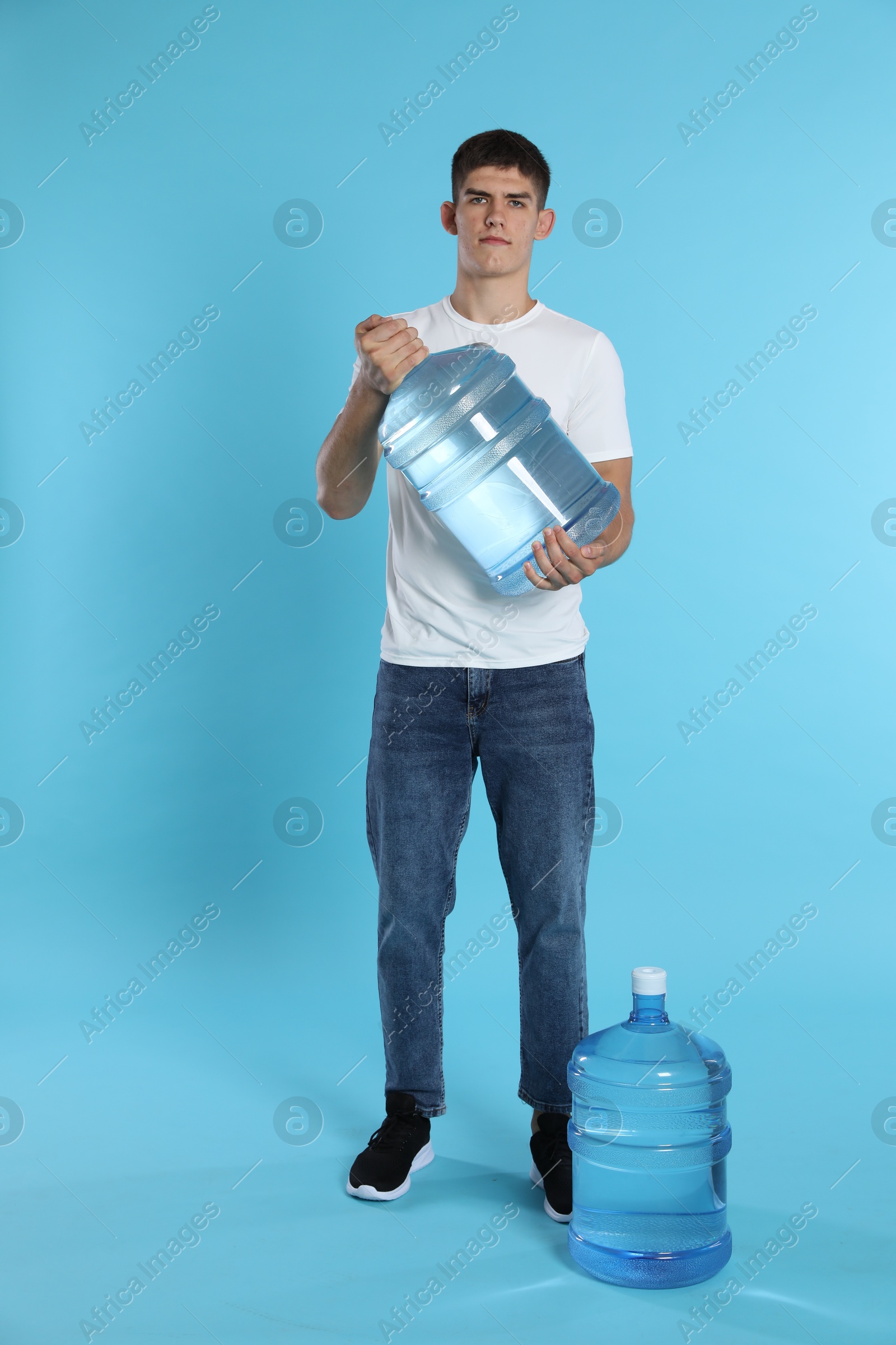 Photo of Delivery man with cooler bottles of water on light blue background