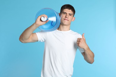 Photo of Delivery man with cooler bottle of water showing thumbs up on light blue background