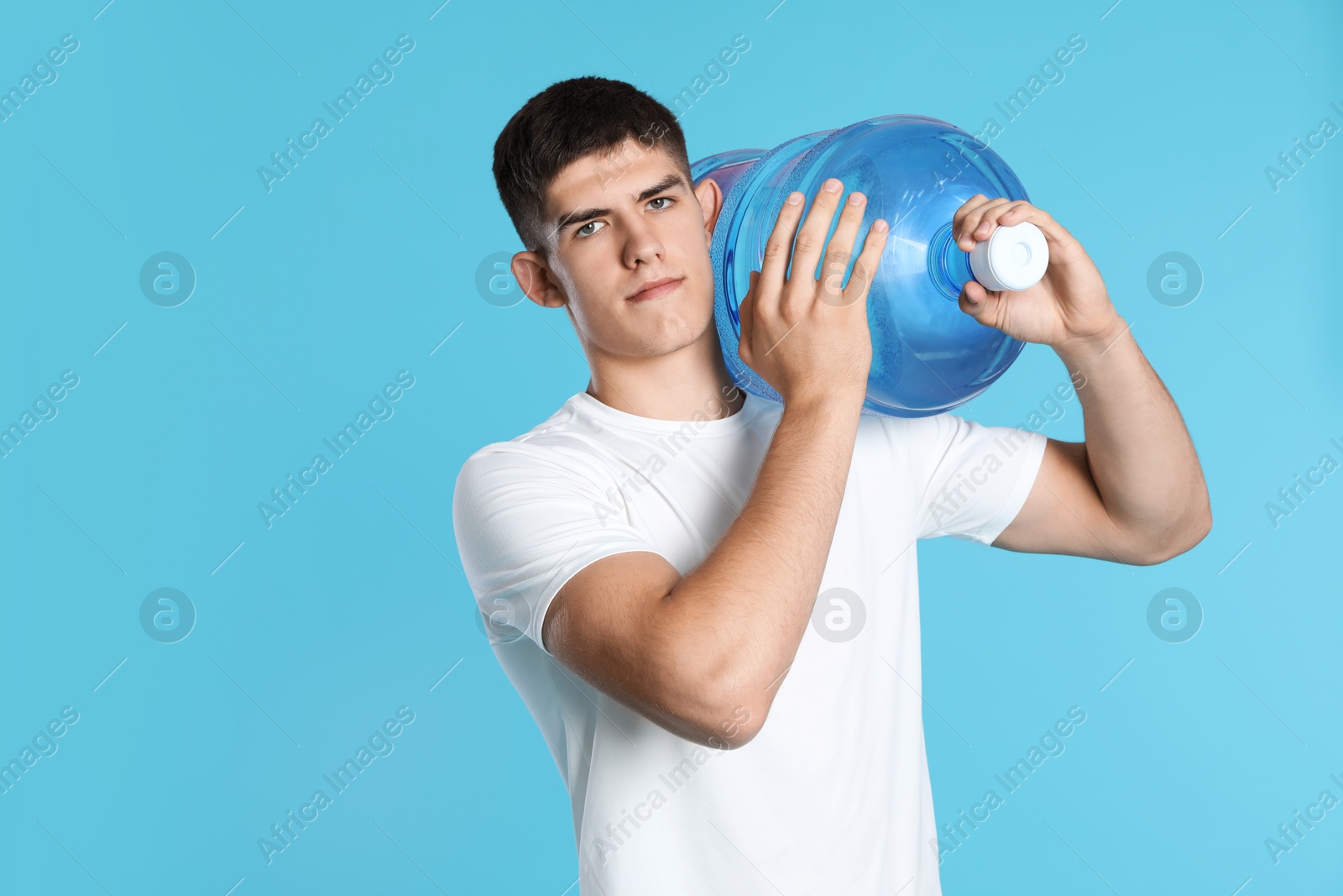 Delivery man with cooler bottle of water on light blue background Photo of Delivery man with cooler bottle of water on light blue background