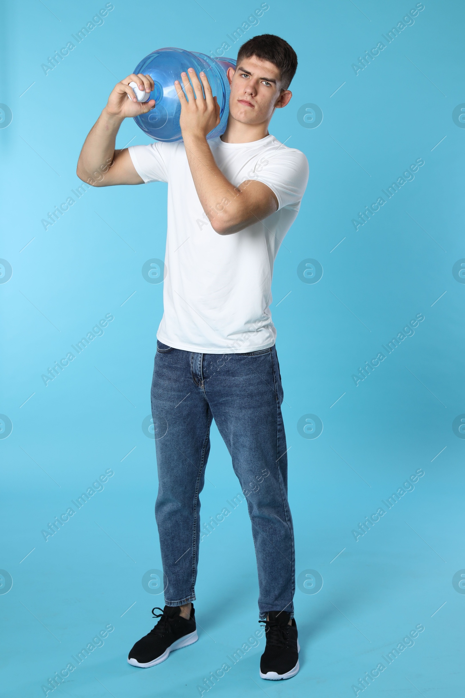 Delivery man with cooler bottle of water on light blue background Photo of Delivery man with cooler bottle of water on light blue background