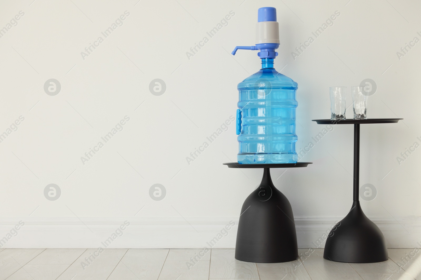 Cooler bottle with water, pump and glasses near white wall. Space for text Photo of Cooler bottle with water, pump and glasses near white wall. Space for text