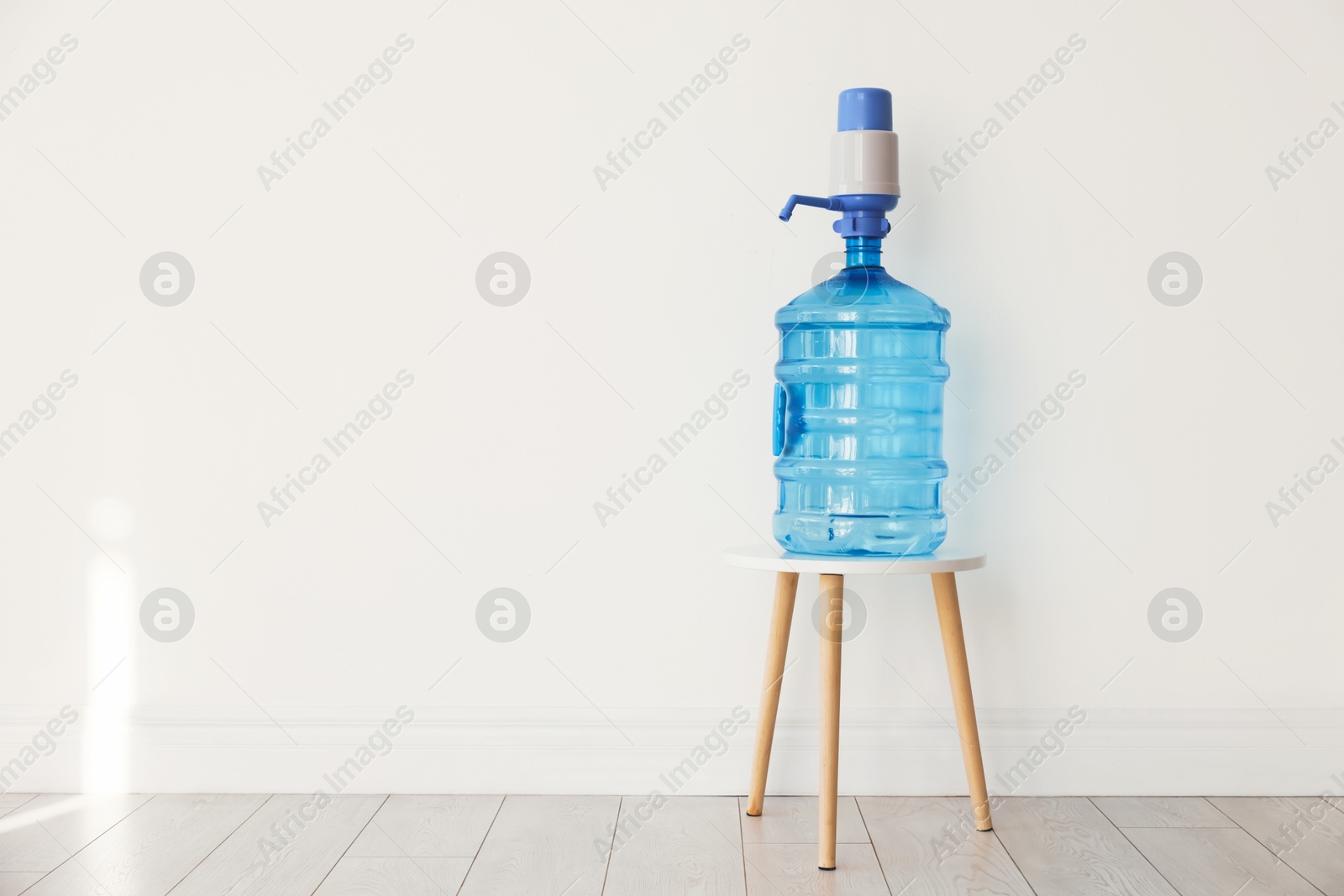Cooler bottle with water and pump near white wall. Space for text Photo of Cooler bottle with water and pump near white wall. Space for text