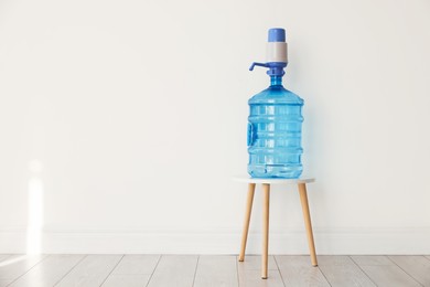 Photo of Cooler bottle with water and pump near white wall. Space for text