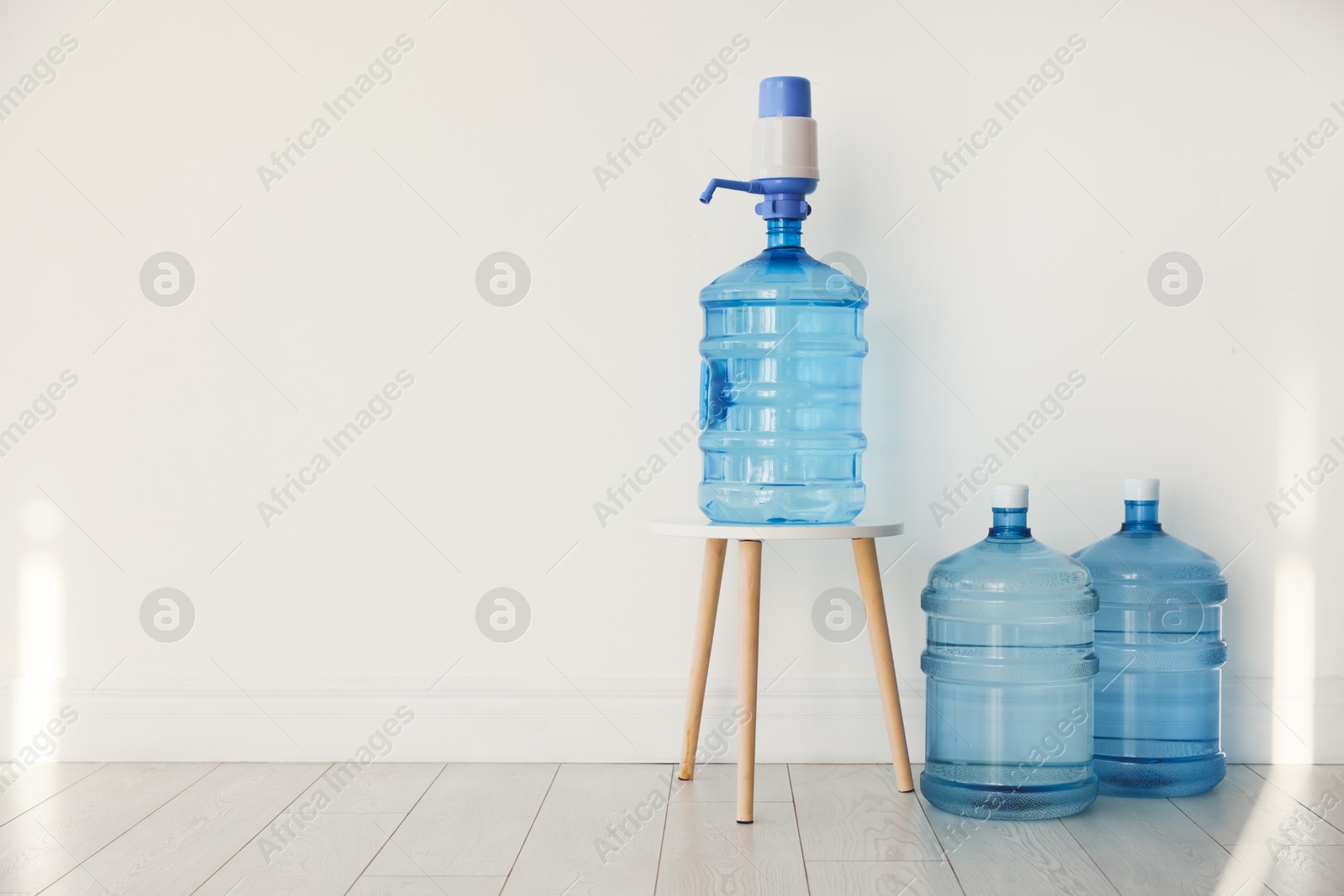 Photo of Cooler bottles with water near white wall. Space for text