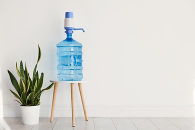 Photo of Cooler bottle with water, pump and houseplant near white wall. Space for text