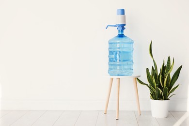 Photo of Cooler bottle with water, pump and houseplant near white wall. Space for text