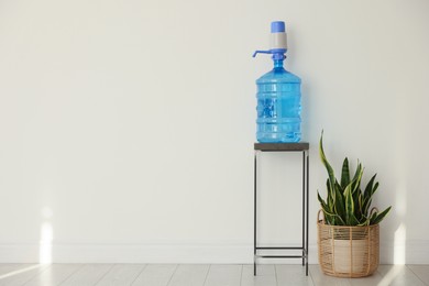 Photo of Cooler bottle with water, pump and houseplant near white wall. Space for text