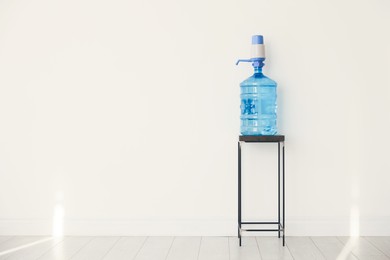 Photo of Cooler bottle with water and pump near white wall. Space for text
