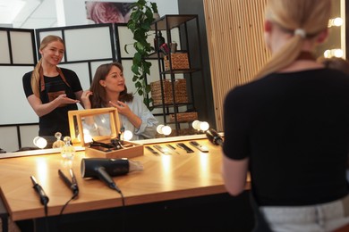 Photo of Hairstylist working with client near mirror in salon