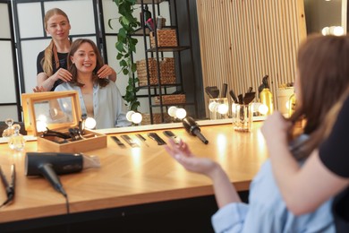 Photo of Hairstylist working with client near mirror in salon