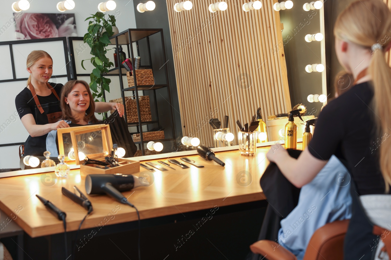 Photo of Hairstylist working with client near mirror in salon