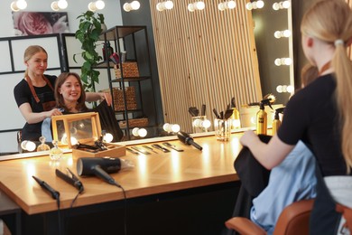Photo of Hairstylist working with client near mirror in salon
