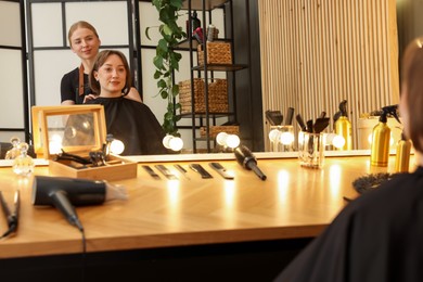 Photo of Hairstylist working with client near mirror in salon