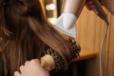 Photo of Hairstylist blow drying client's hair in salon, closeup