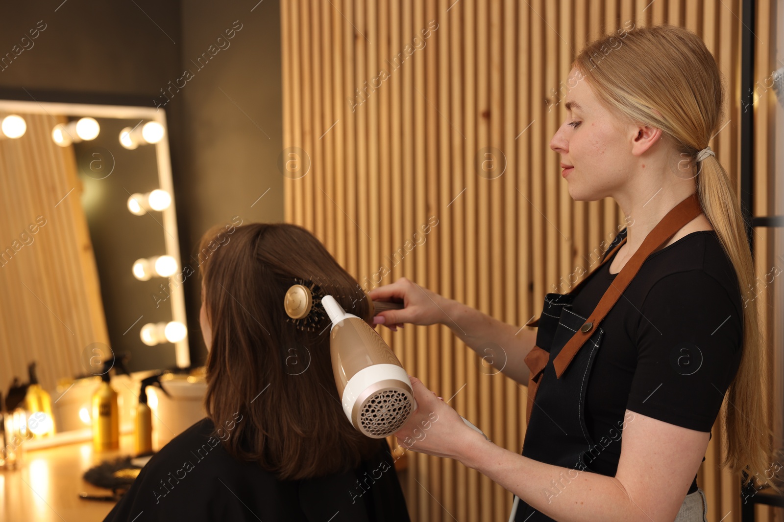 Hairstylist blow drying client's hair in salon Photo of Hairstylist blow drying client's hair in salon