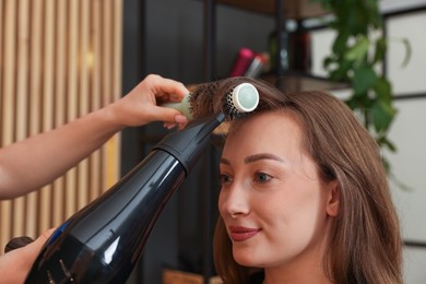 Photo of Hairstylist blow drying client's hair in salon, closeup