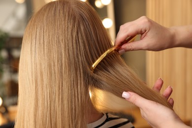 Photo of Hairstylist combing woman's hair in salon, closeup