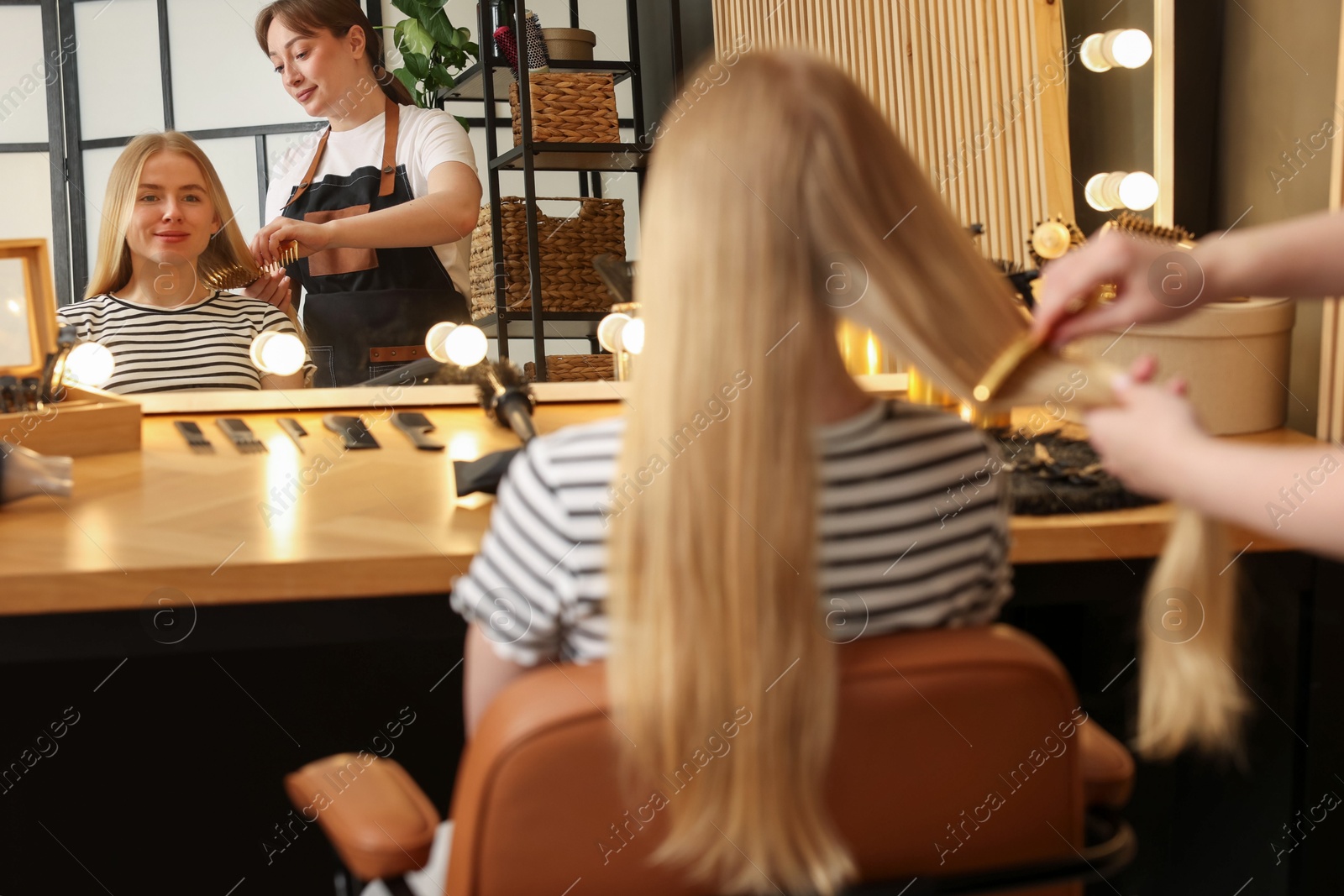 Professional hairstylist combing woman's hair in salon Photo of Professional hairstylist combing woman's hair in salon