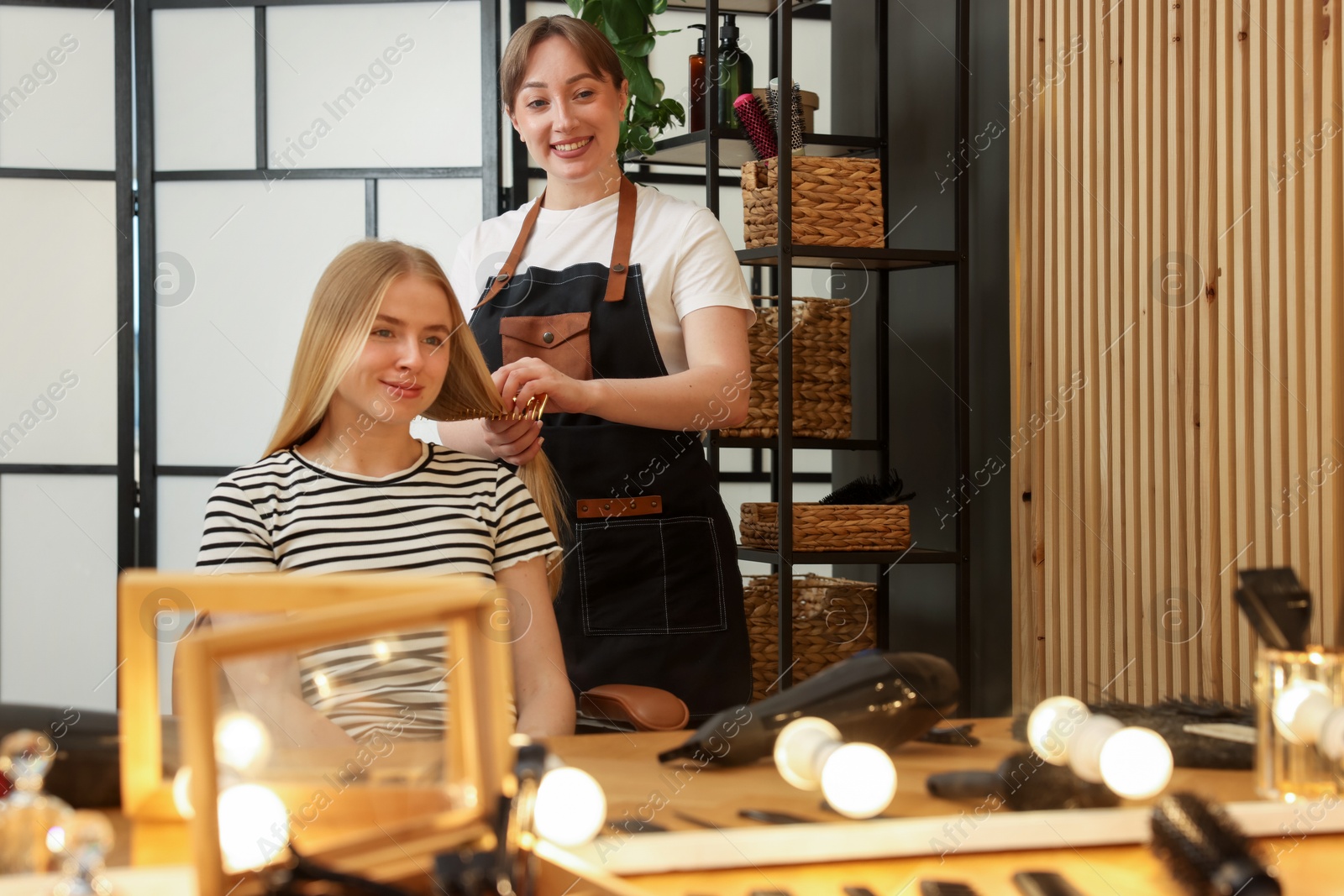 Professional hairstylist combing woman's hair in salon Photo of Professional hairstylist combing woman's hair in salon