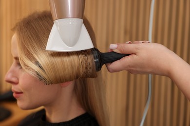 Photo of Hairstylist blow drying client's hair in salon, closeup