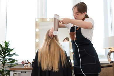 Photo of Hairstylist blow drying client's hair in salon