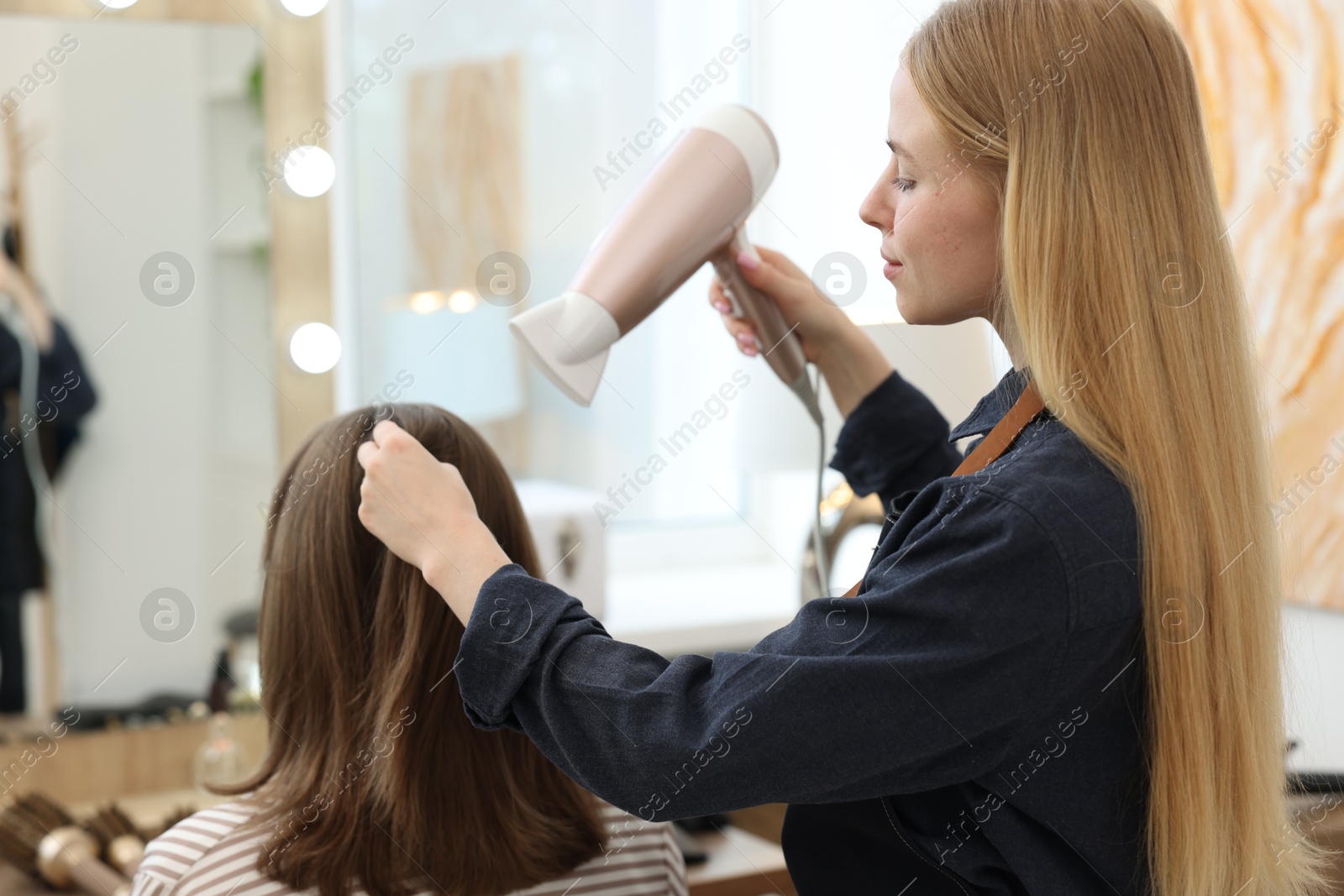 Photo of Hairstylist blow drying client's hair in salon