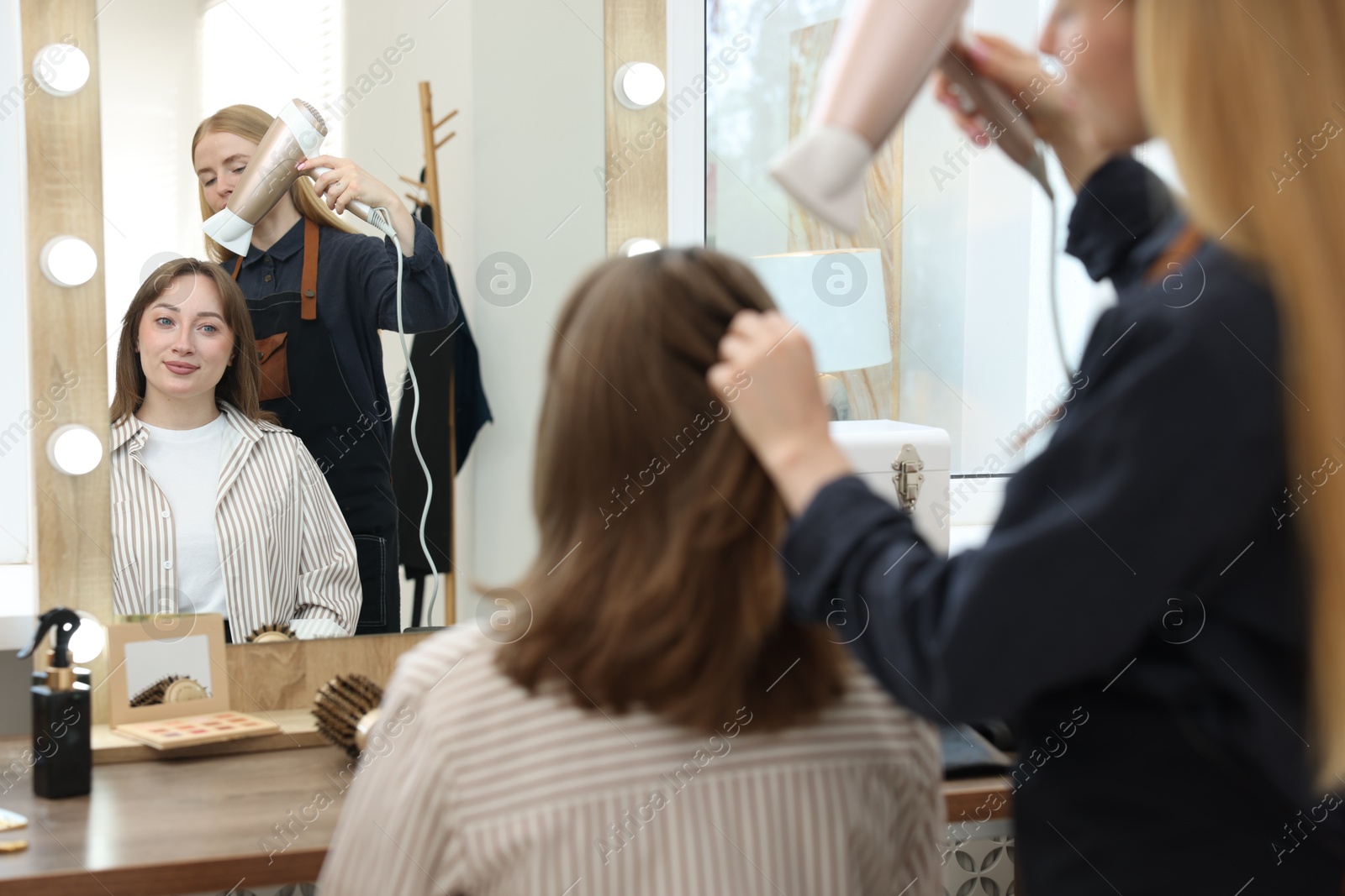 Photo of Hairstylist blow drying client's hair in salon, closeup