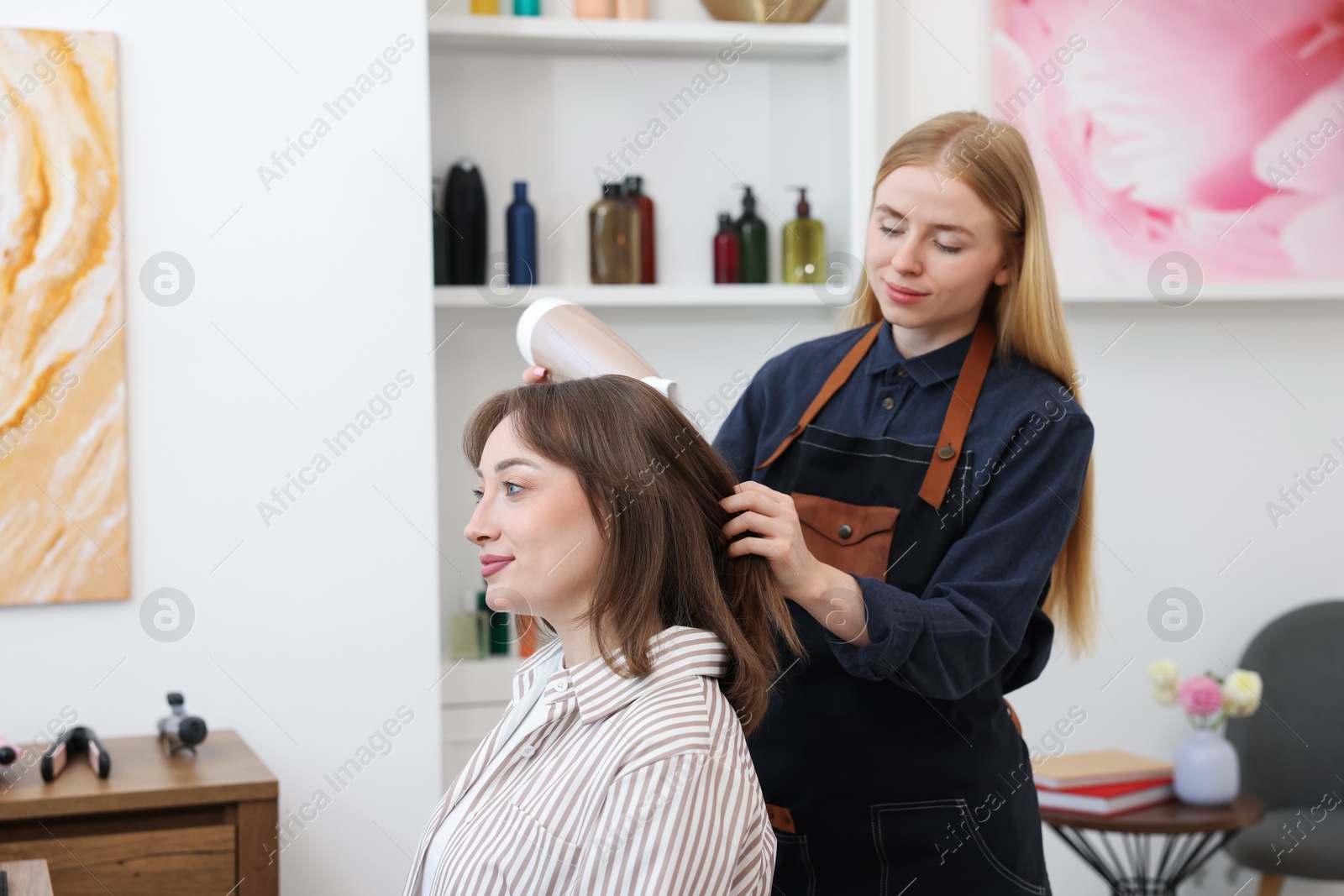 Photo of Hairstylist blow drying client's hair in salon