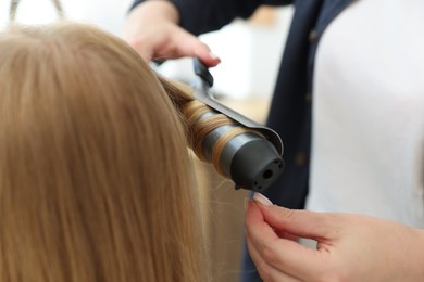 Photo of Hairstylist curling woman's hair in salon, closeup