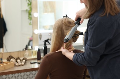Photo of Professional hairstylist curling woman's hair in salon, closeup