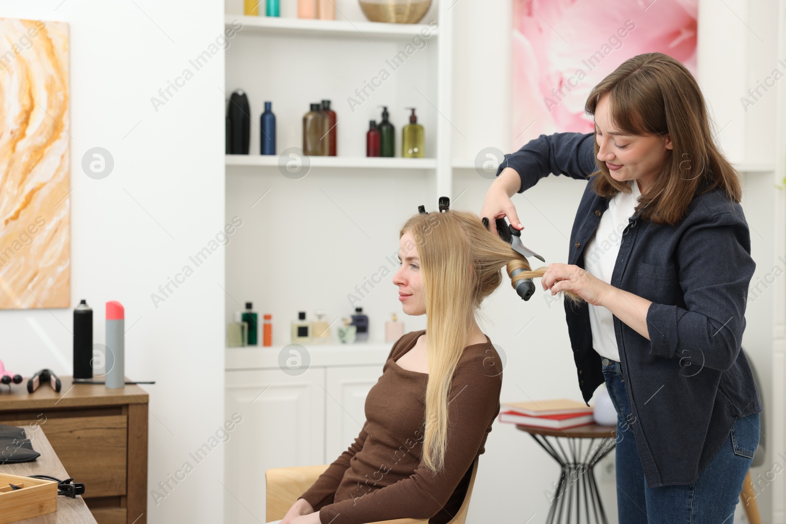 Photo of Professional hairstylist curling woman's hair in salon