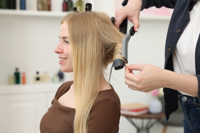 Photo of Professional hairstylist curling woman's hair in salon, closeup