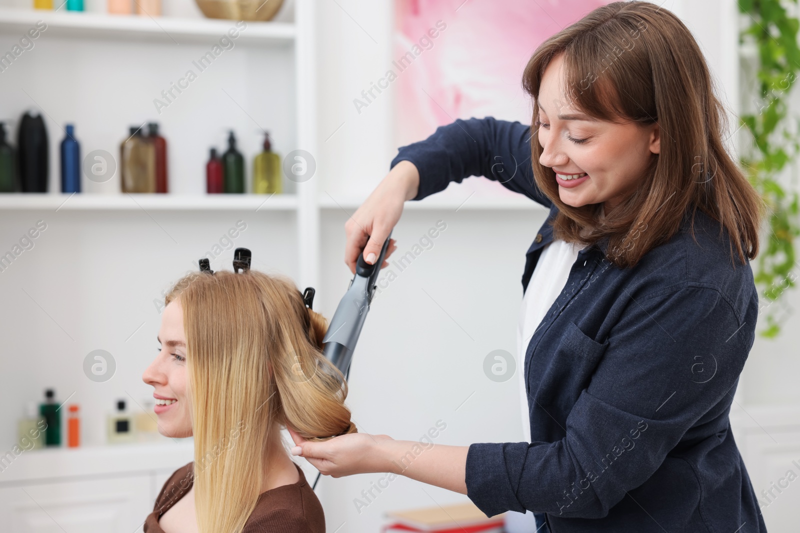 Photo of Professional hairstylist curling woman's hair in salon