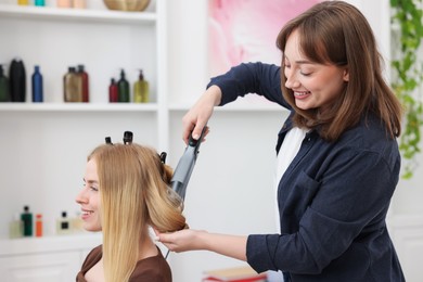 Photo of Professional hairstylist curling woman's hair in salon