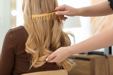 Photo of Professional hairstylist combing woman's hair in salon, closeup