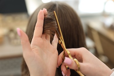 Photo of Hairstylist cutting client's hair with scissors in salon, closeup