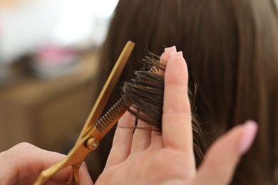 Photo of Hairstylist cutting client's hair with scissors in salon, closeup