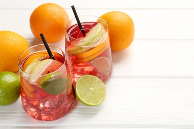 Photo of Tasty punch with ice, mint and slices of fruits in glasses on white wooden table, closeup with space for text. Refreshing drink