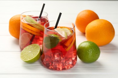 Photo of Tasty punch with ice, mint and slices of fruits in glasses on white wooden table, closeup. Refreshing drink